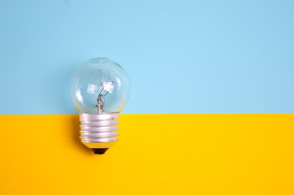 A lightbulb lying on a background that is horizontally half blue and half yellow.