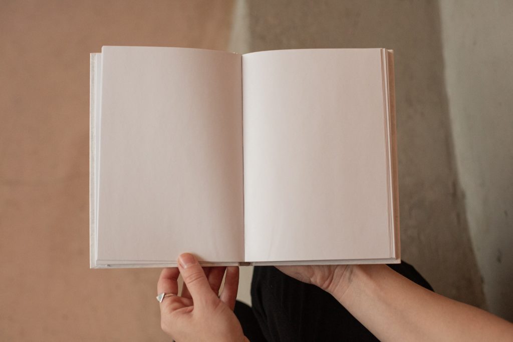 An open white book with blank pages is held by a pair of hands.