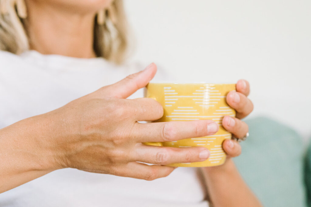 Hands of a copywriter holding a mustard yellow patterned teacup