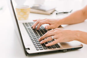 Hands copywriting on a laptop with yellow mug in the background