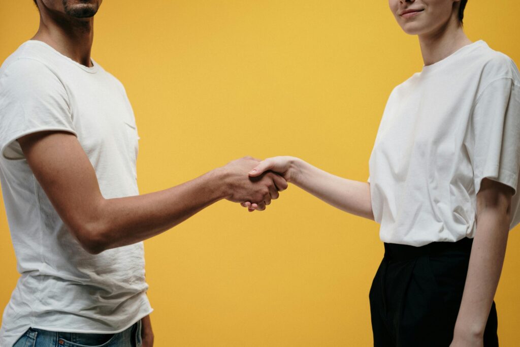 Man and woman standing opposite each other shaking hands with a yellow background