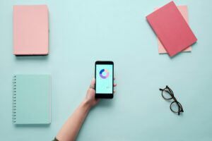 Hand holding a smartphone with analytics data, surrounded by notepads and a blue background